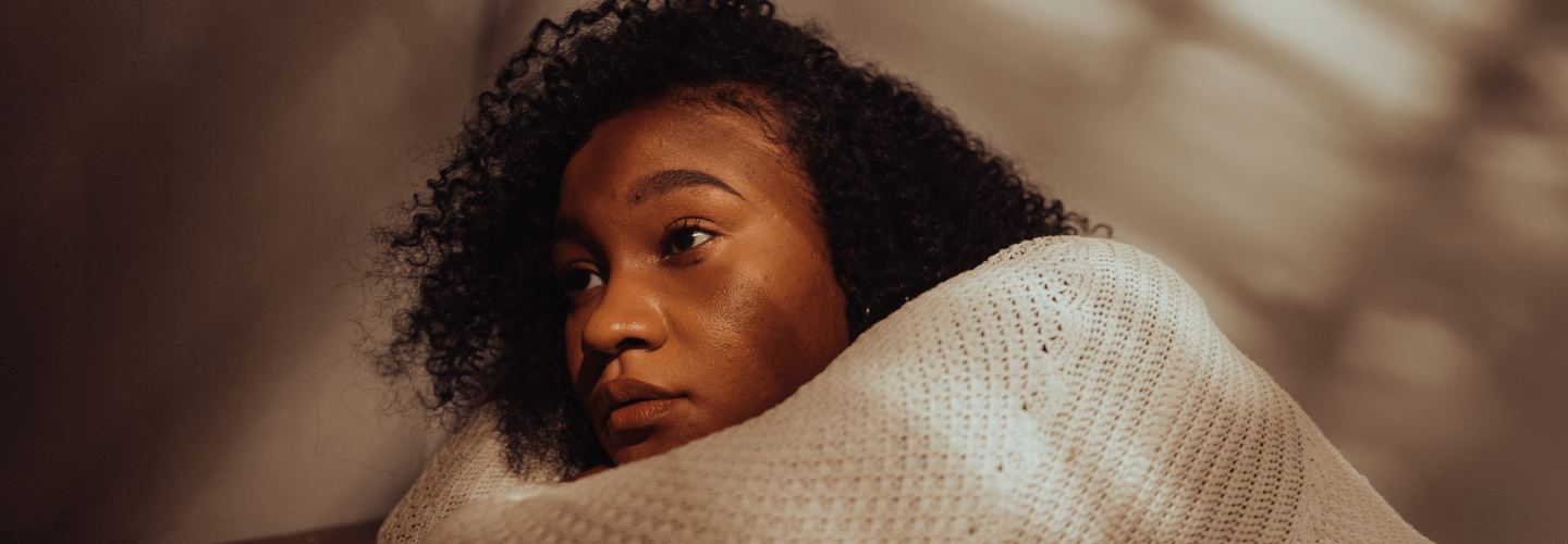 Woman wrapped in a blanket showing the quiet signs of emotional exhaustion from overgiving and chronic emotional burnout.